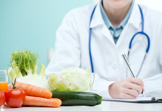 médico de nutrologia escrevendo em uma mesa com alguns alimentos ao lado