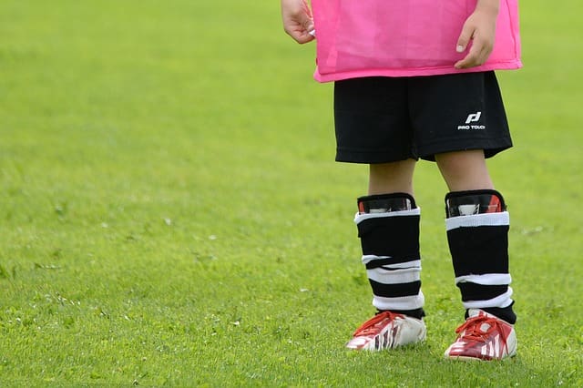 parte inferior de criança com roupa de futebol em um campo, combatendo o sedentarismo