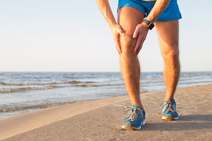 homem com as mãos no joelho após correr na praia, devido osteoartrite de joelho