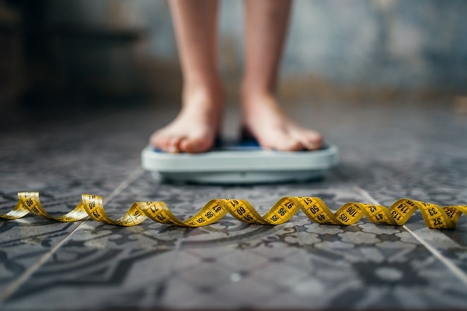pés de pessoa com obesidade em cima de de balança com fita métrica na frente