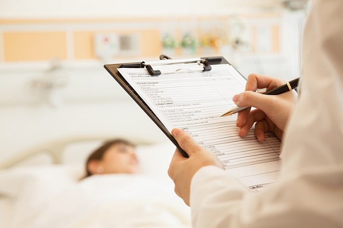 médico anotando em prancheta com paciente com coronavírus ao fundo