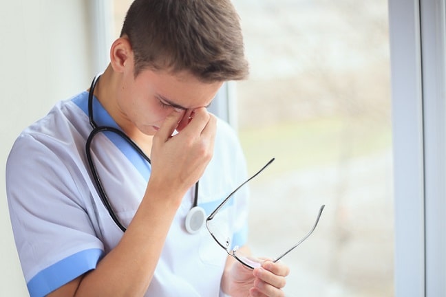 médico com o óculos em uma mão e a outra mão no rosto, com ansiedade na covid-19