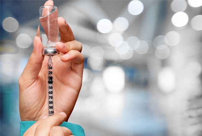 mão de médico segurando dose de vacinas contra a Covid-19, como Pfizer ou Janssen