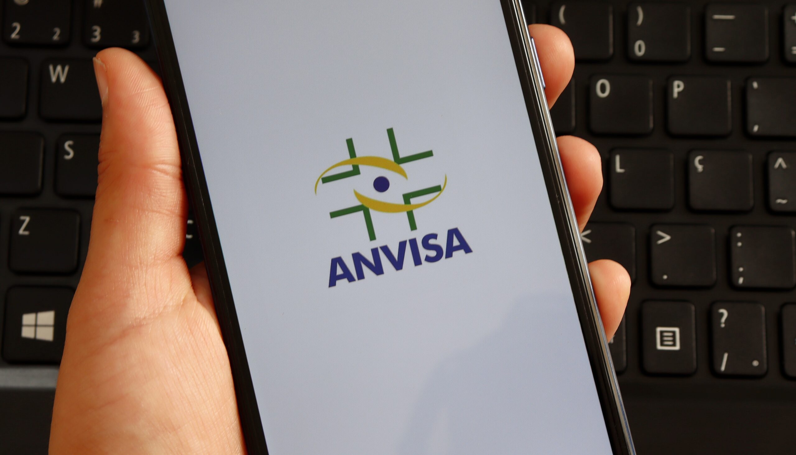 Destaque do nome e logo da Anvisa em um smartphone na mão de uma pessoa